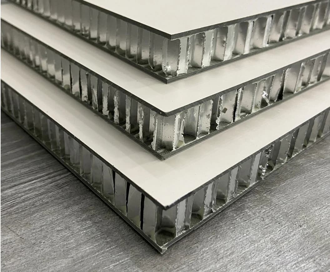 Tres paneles honeycomb blancos vistos de canto: el núcleo de panal de aluminio entre las dos caras de SPC