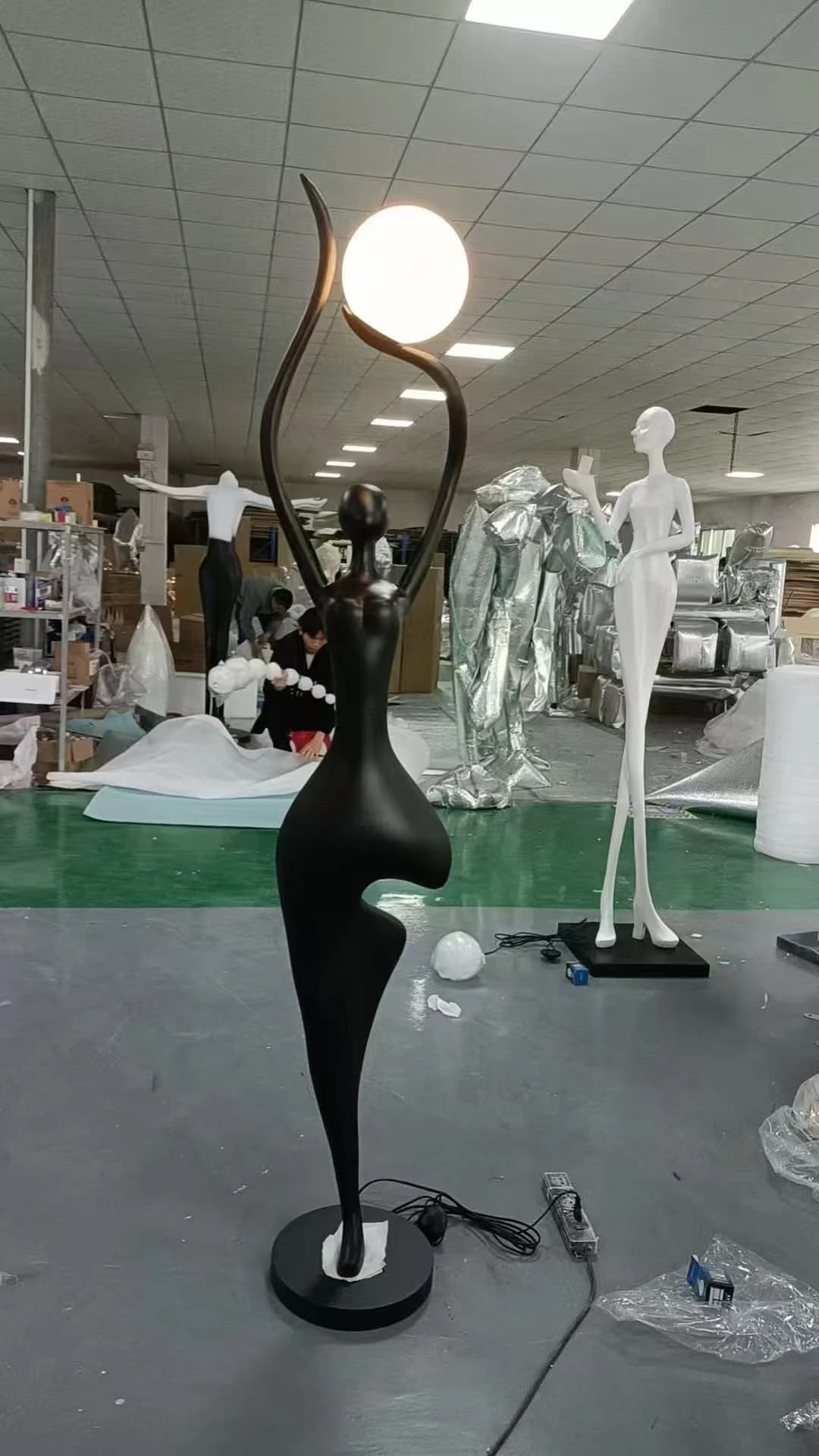 Escultura de figura negra estirada con globo de luz