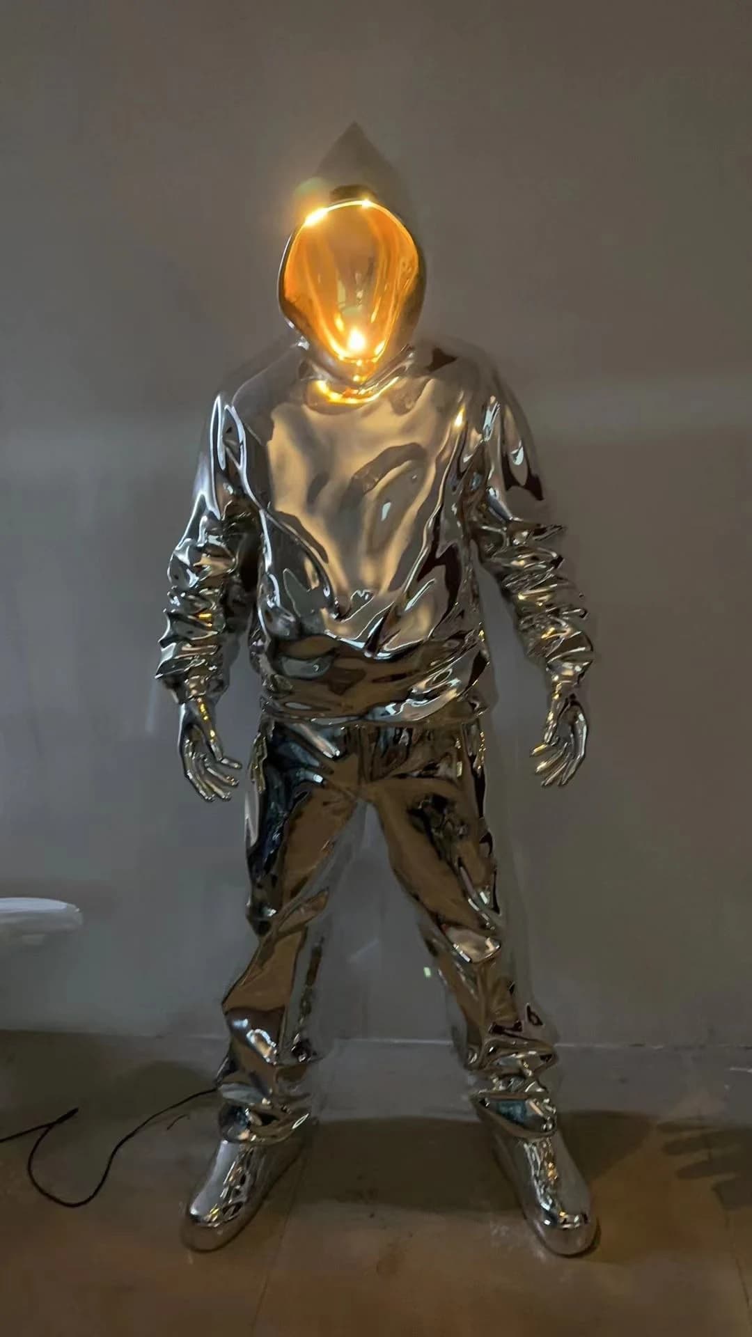 Escultura de figura con capucha plateada y casco iluminado