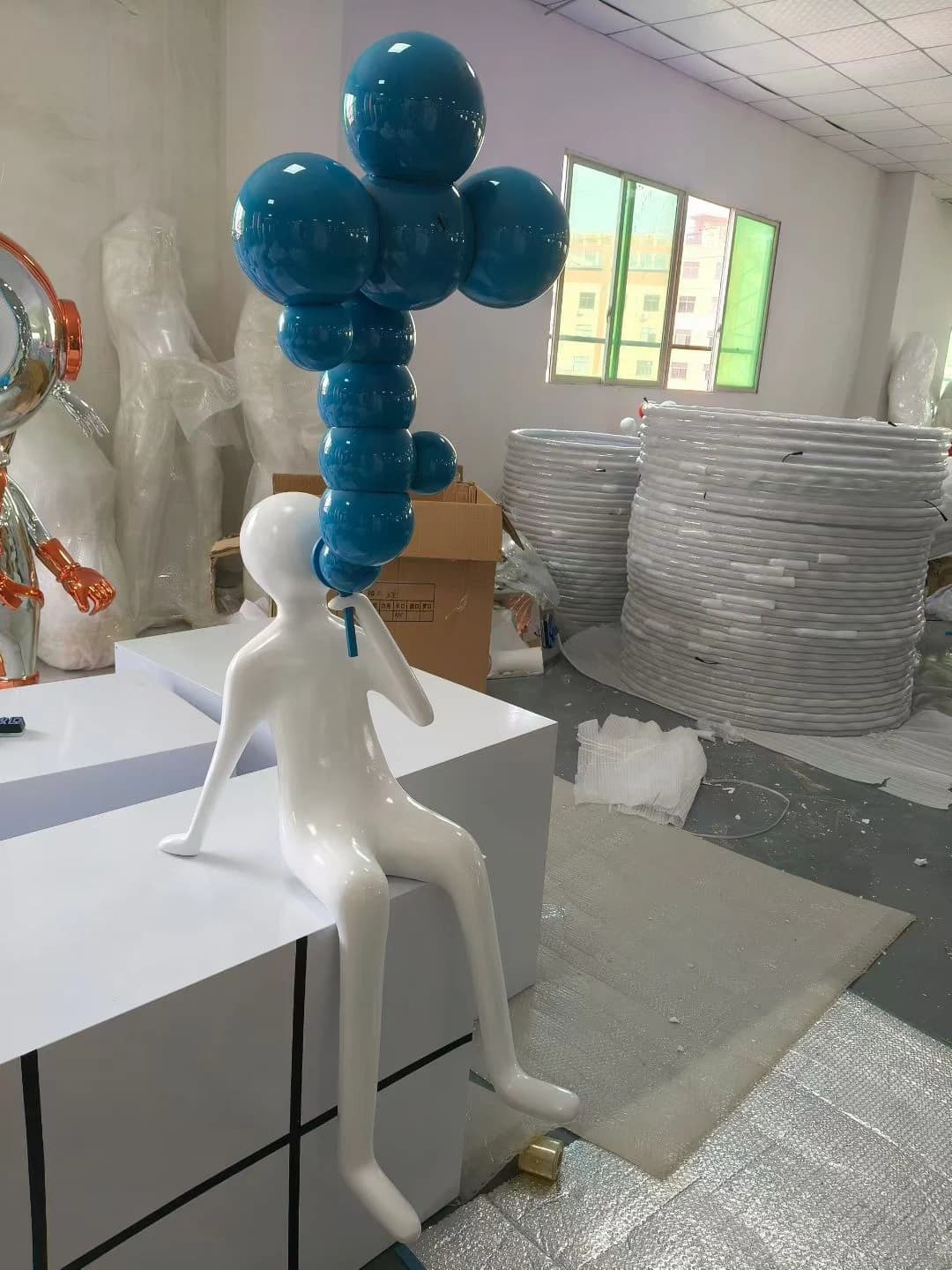 Escultura de figura blanca sentada con globos azules