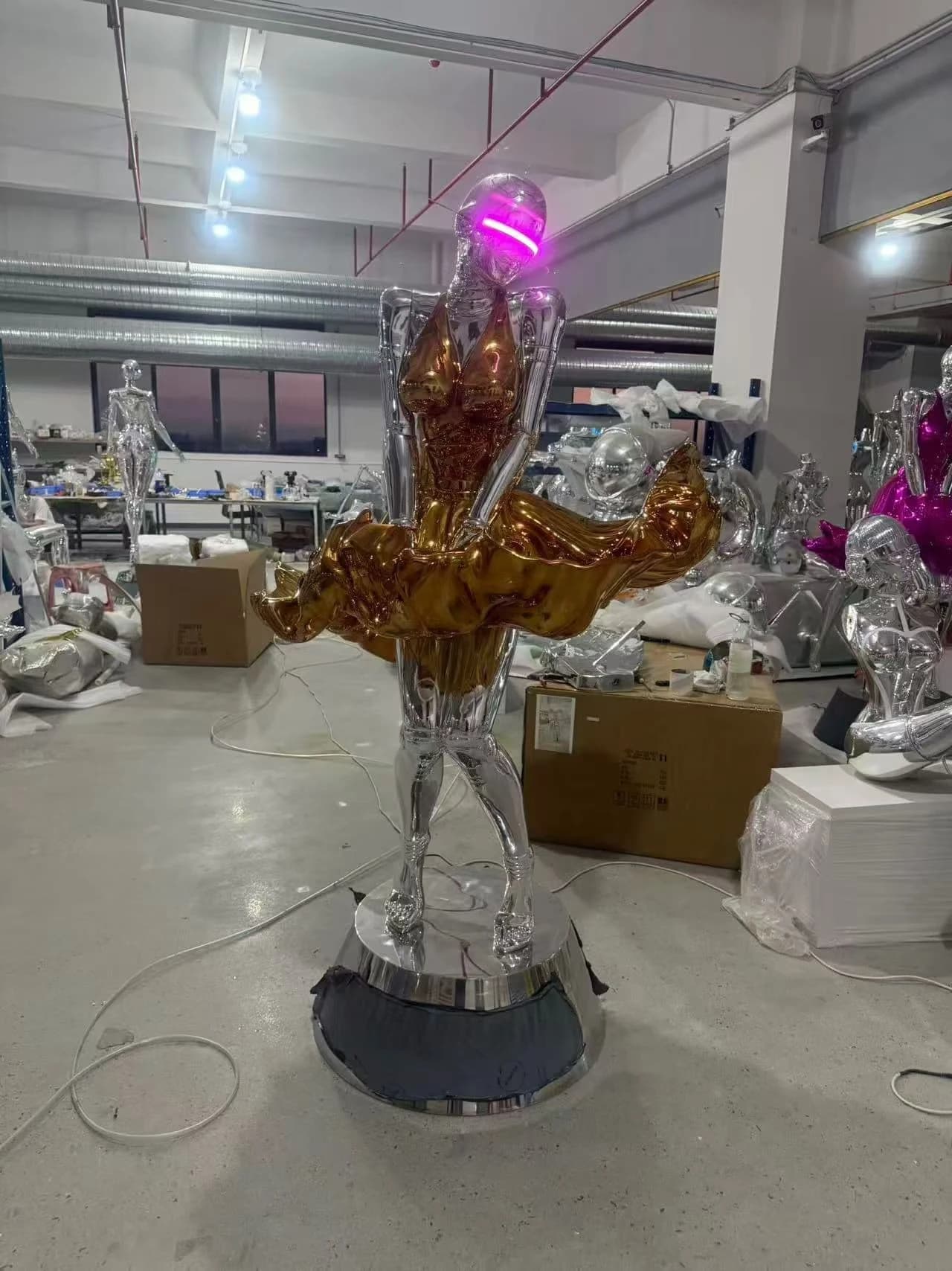 Escultura de figura plateada con falda dorada y luz violeta en la cabeza, sobre base redonda