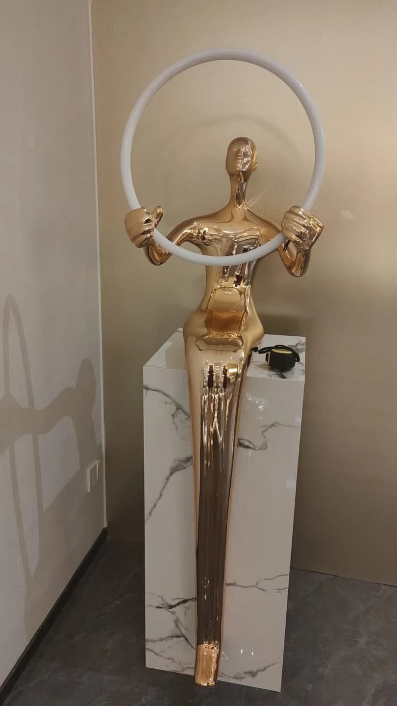 Escultura de figura dorada con aro sobre pedestal