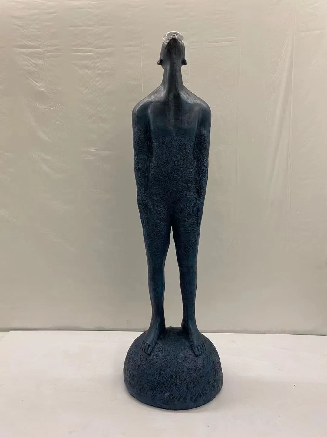 Escultura de figura de pie sobre esfera, color azul petróleo